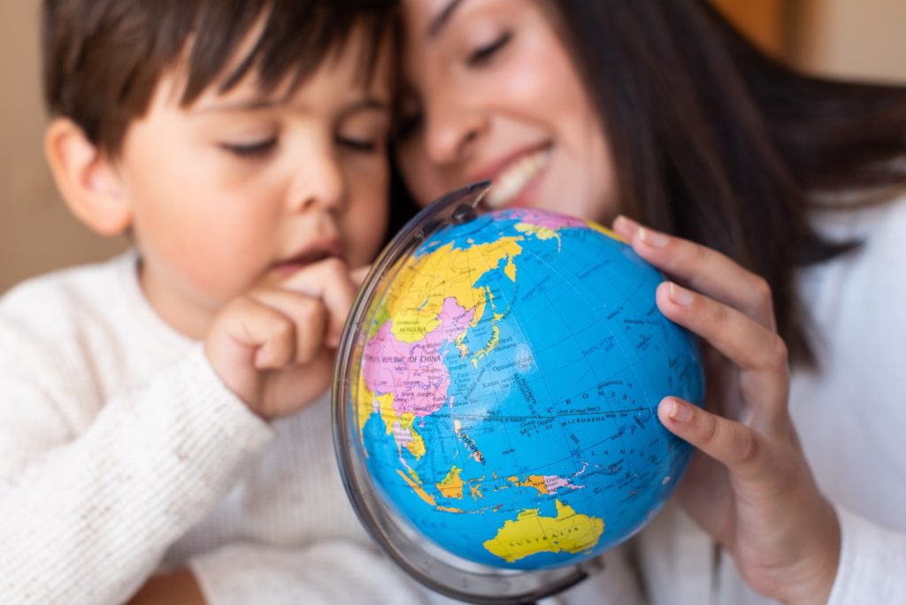 Preschooler Kid learing geography with a globe map and teacher educador help. Homeshooling.