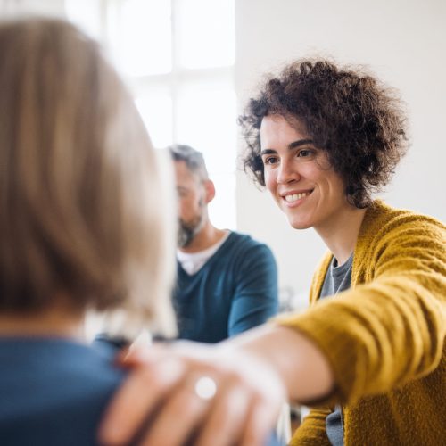 Serious men and women sitting in a circle during group therapy, supporting each other.