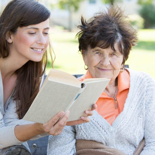 Junge Frau ließt Seniorin ein Buch vor