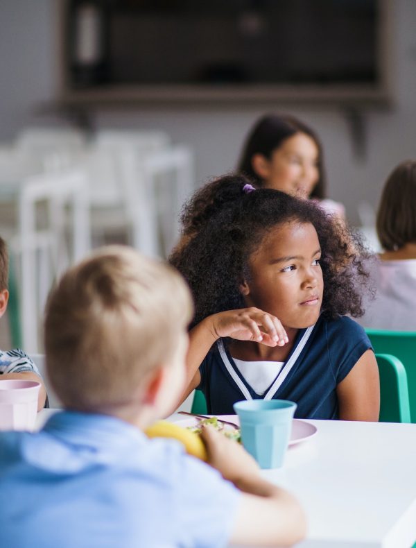 A group of cheerful small school kids in canteen, eating lunch. A group of cheerful small school kids in canteen, eating lunch.
