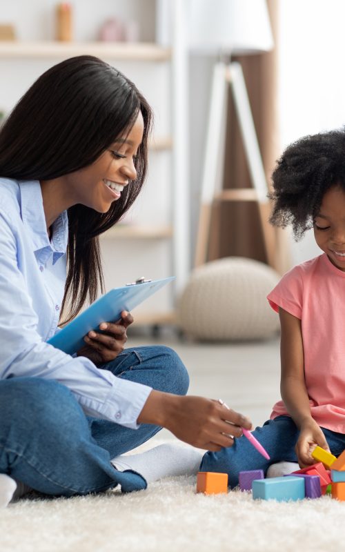 Adorable black kid and child psychotherapist playing with bricks