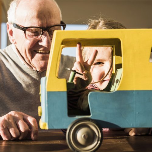 Grandfather and granddaughter assembling toy bus, girl making victory sign