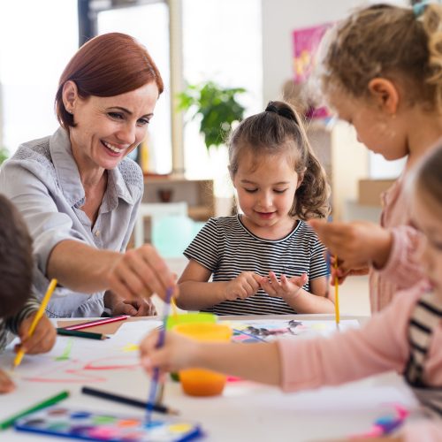 Group of small nursery school children with teacher indoors in classroom, painting