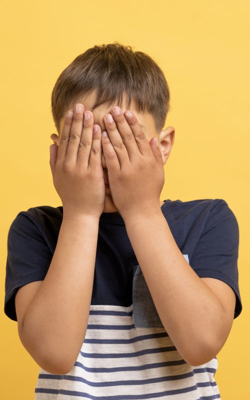 Shy little boy feeling ashamed, cover face with palms