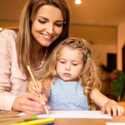 smiling educator helping kid drawing in kindergarten